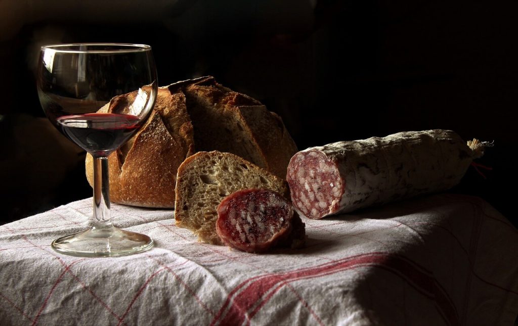 A tasteful composition featuring a glass of wine gracefully placed on a table, accompanied by freshly baked bread and slices of fuet, a cured meat delicacy. 